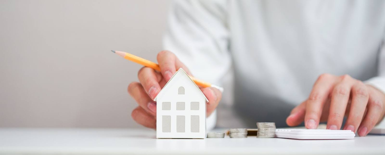 A man working on paper work with a paper house sitting in front of him to represent him filing an insurance claim